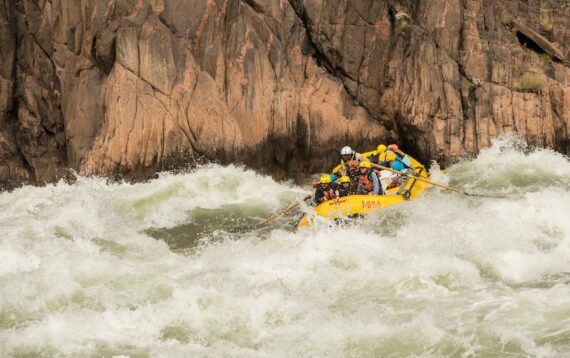 Guests on a Grand Canyon rafting trip ride a raft through a huge wave