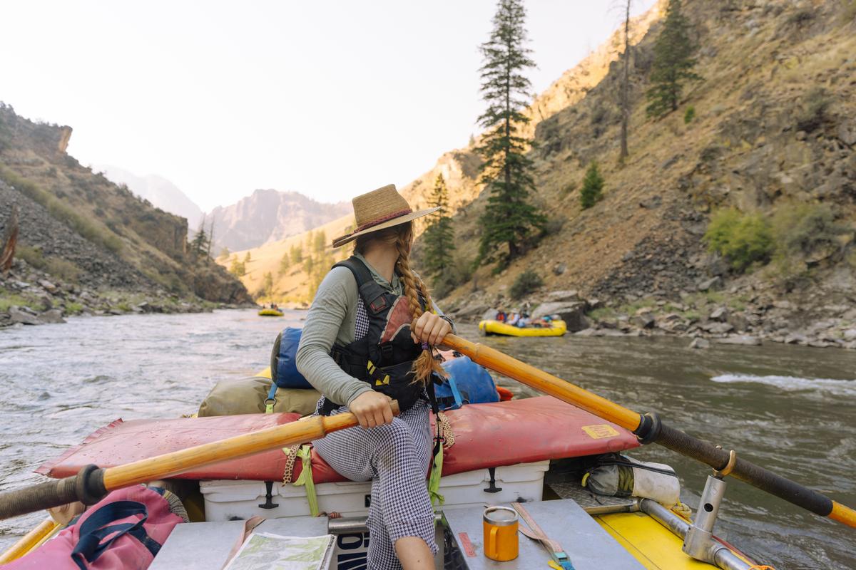 A woman rows an oar boat down a scenic Idaho river canyon