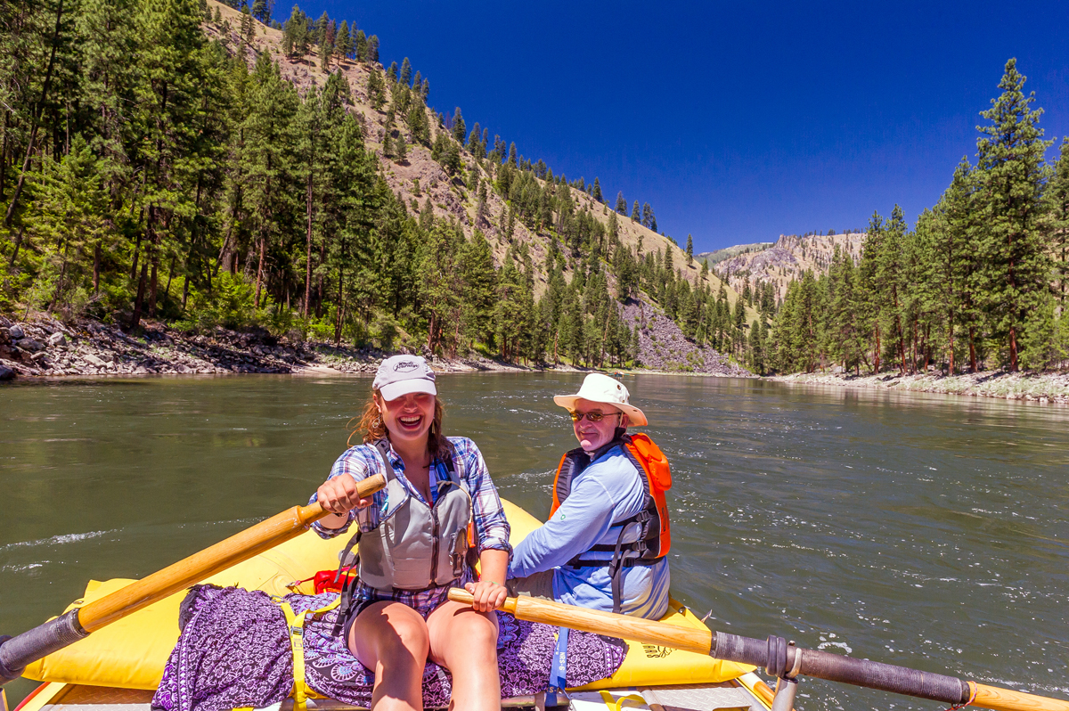 A female river guide smiles brightly as she rows a male passenger down Idaho's Main Salmon River.