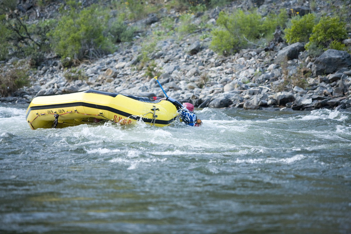 A swimmer hangs on to an upside down boat in a river current