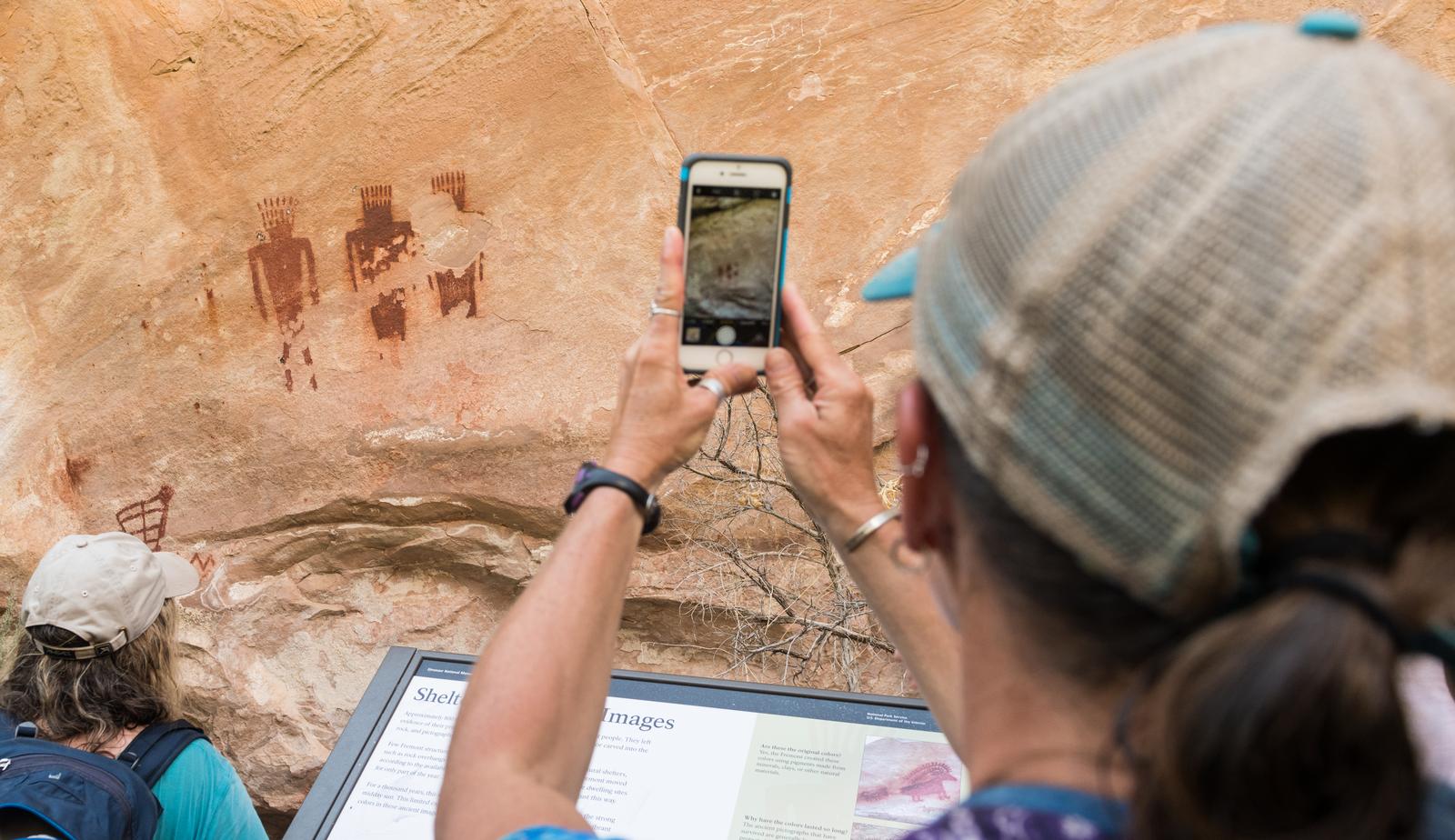 A woman using a smart phone in a case to photograph petroglyphs