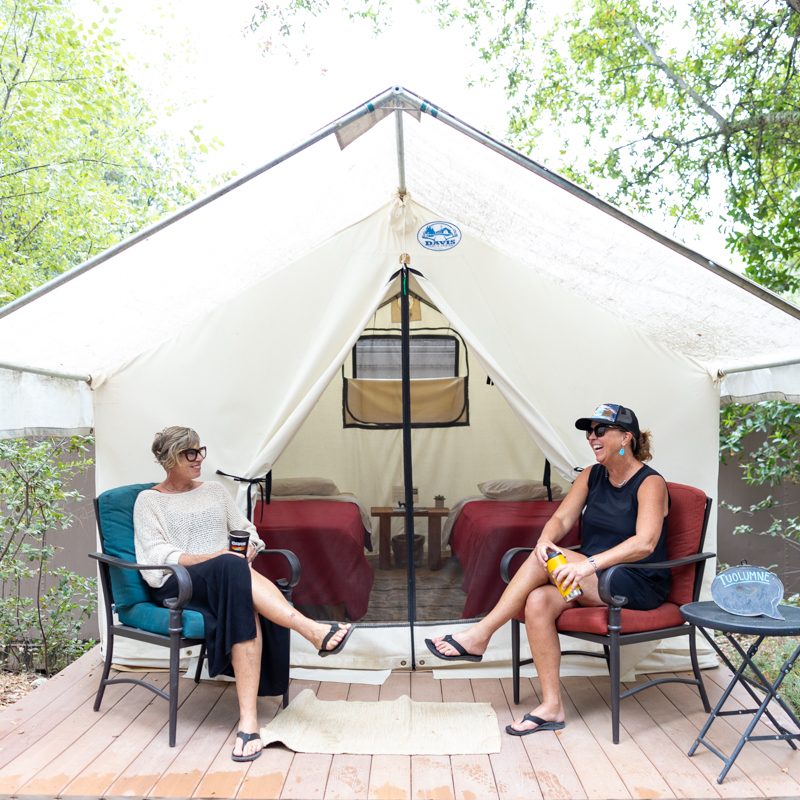 Two women enjoy the deck of a platform tent at the OARS American River Outpost