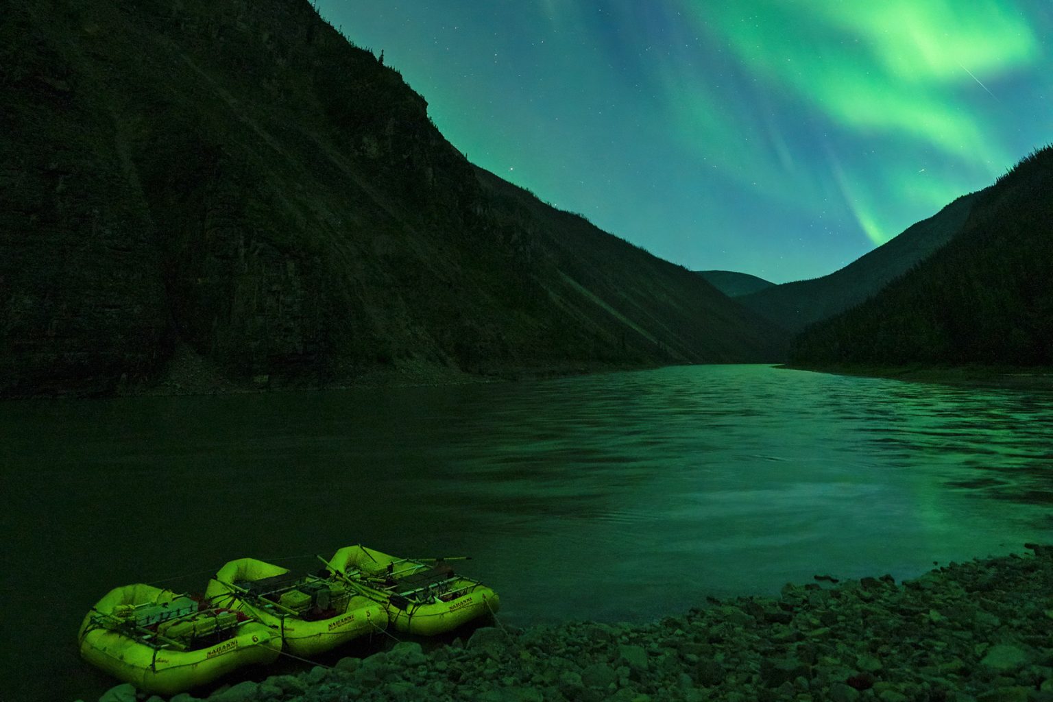 Yellow rafts at shore under the glowing green Northern Lights.