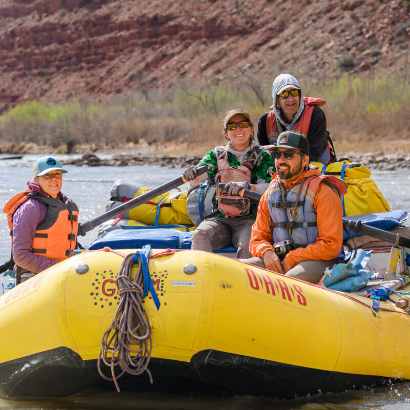 Four adults smile on a yellow raft as they float down the San Juan River on an OARS trip.
