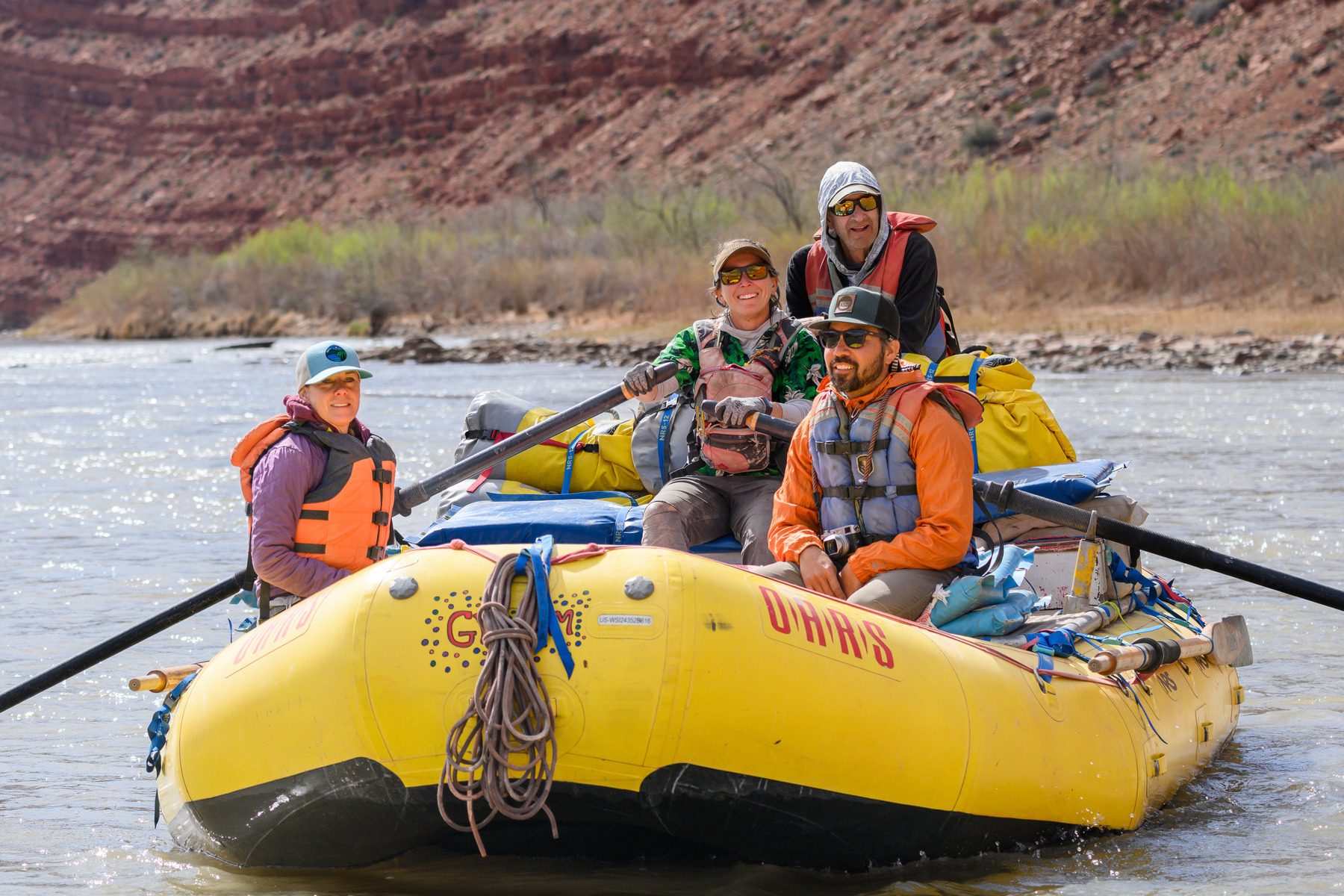 Four adults smile on a yellow raft as they float down the San Juan River on an OARS trip.