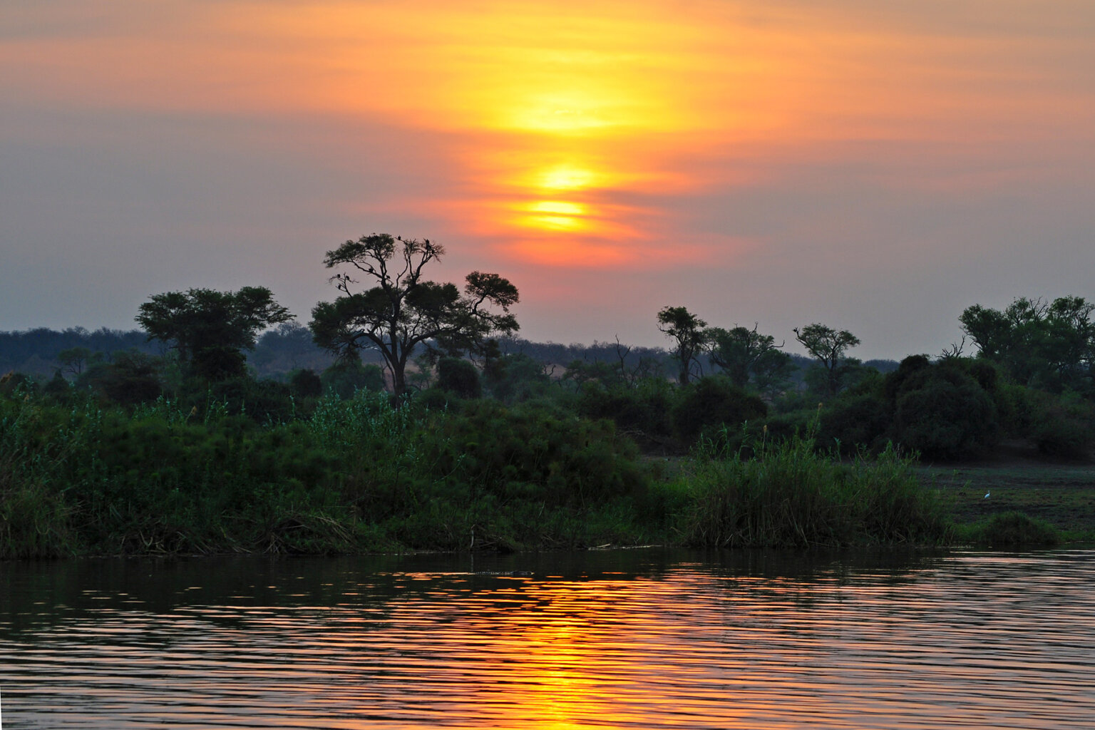 A vibrant sunset reflects off the water backed by lush land.
