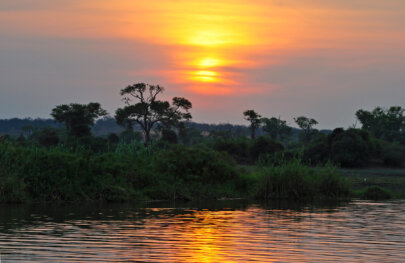 A vibrant sunset reflects off the water backed by lush land.