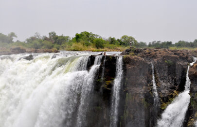 People lounge in a small pool aside the top of a massive waterfall in Afica.