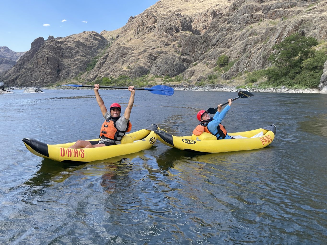 Bruce and Scott hold their kayak paddles in the air while inflatable kayaking. 