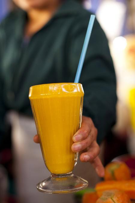 A close-up image of a yellow smoothie in a glass with a straw