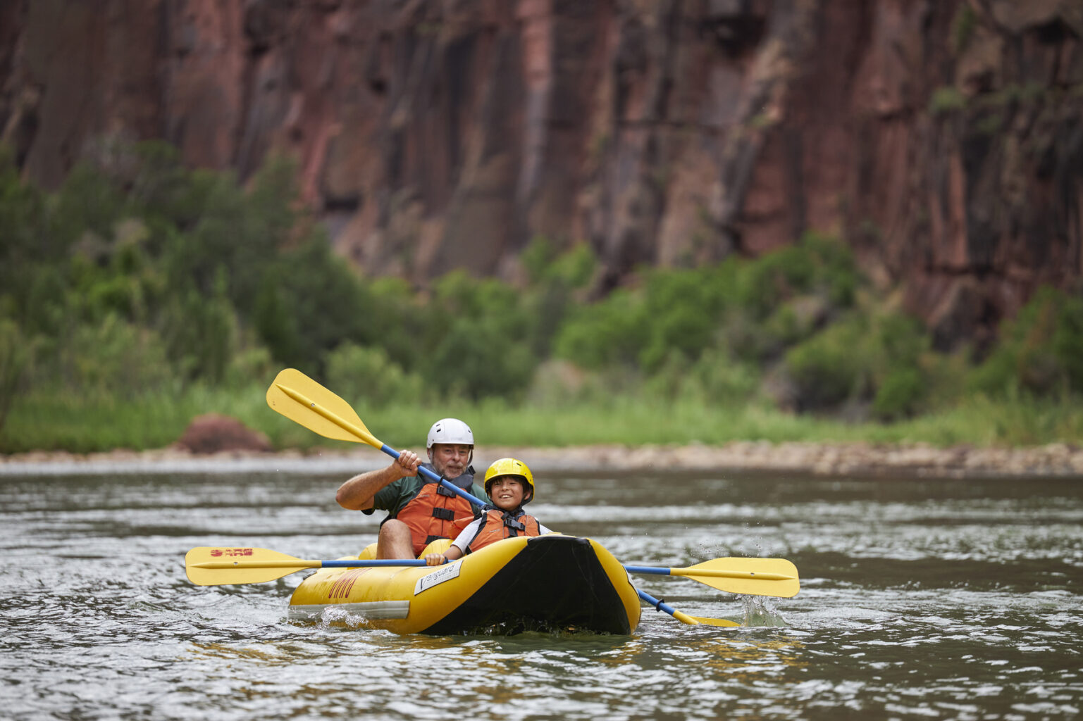 A older man and a boy paddle an inflatable kayak together  