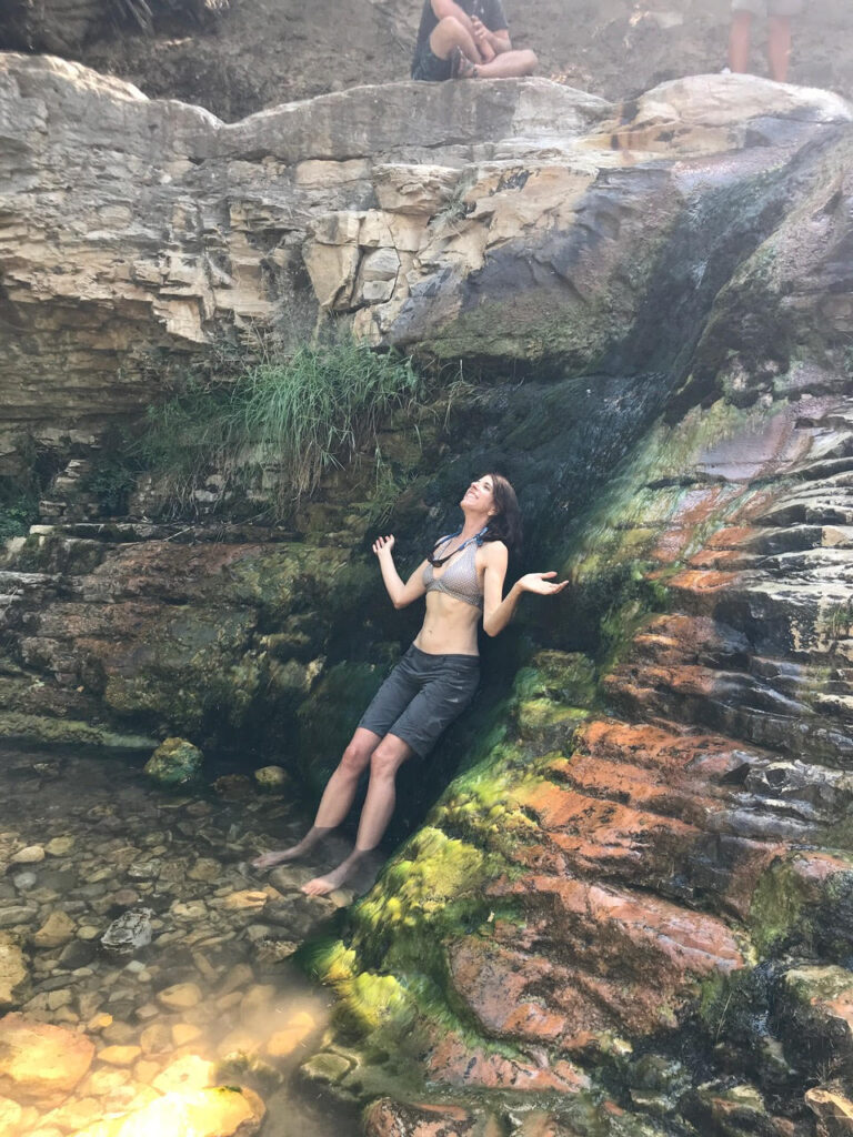 A woman stands beneath a creekside waterfall