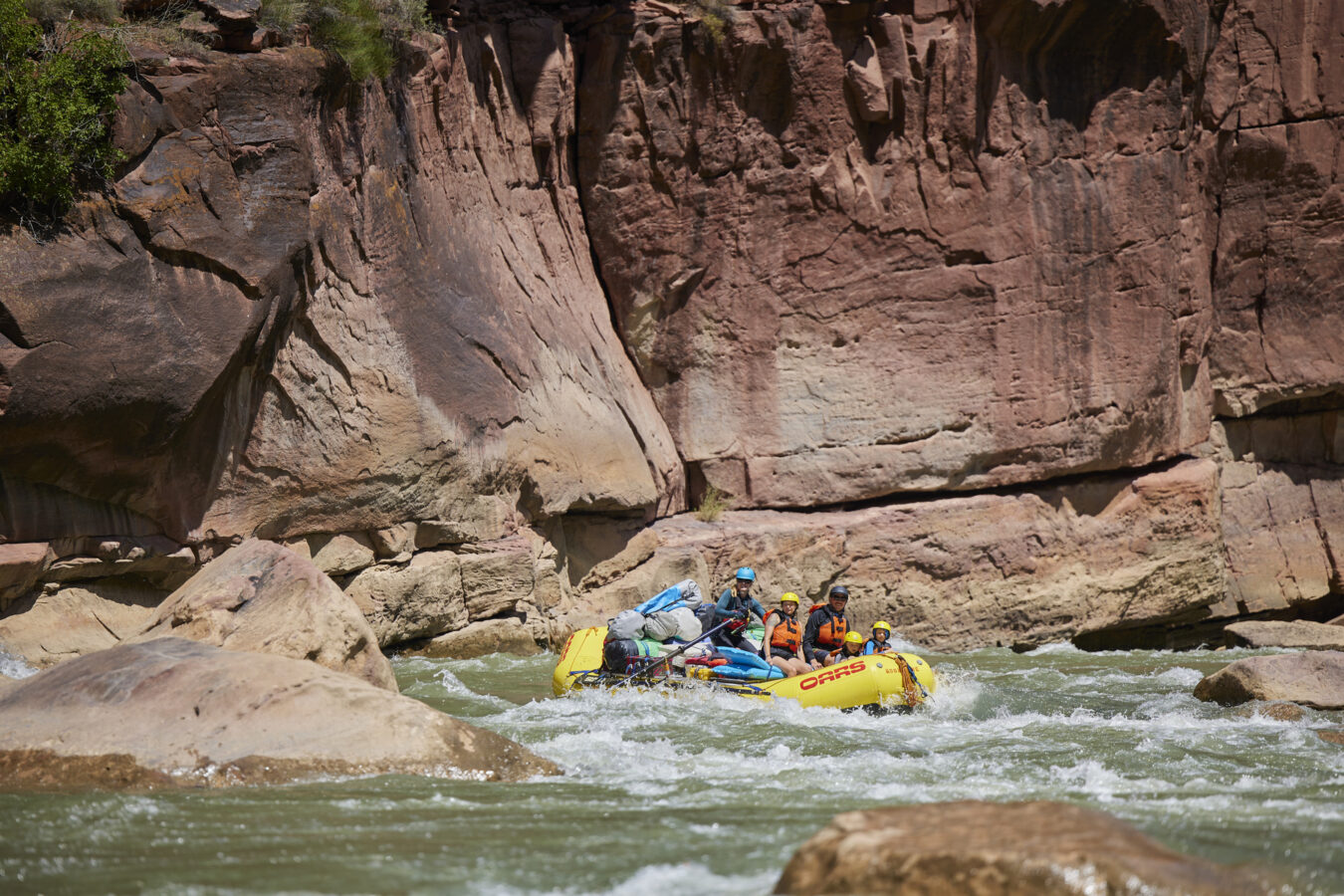 A yellow raft navigates through a rocky section of the Green River on a Gates of Lodore rafting trip. Stunning red rock walls tower in the background.