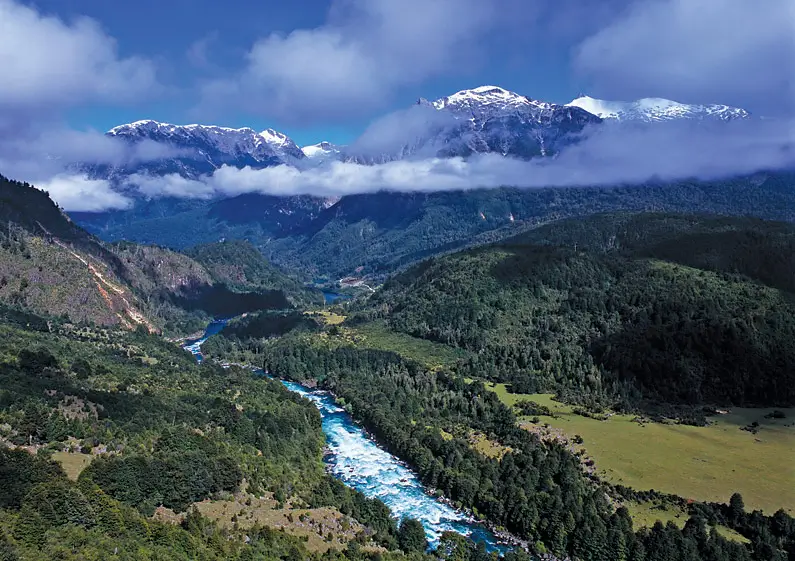 An aerial view of a famous stretch of whitewater, along the Futaleufu River in Chile. There are snow-capped peaks in the distance and the river is surrounded by forest.