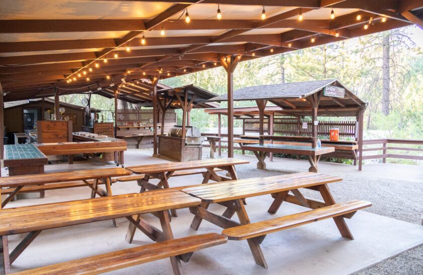 A shot of empty picnic tables under a wooden structure with the buffet serving areas behind them at OARS at EarthTrek campground.