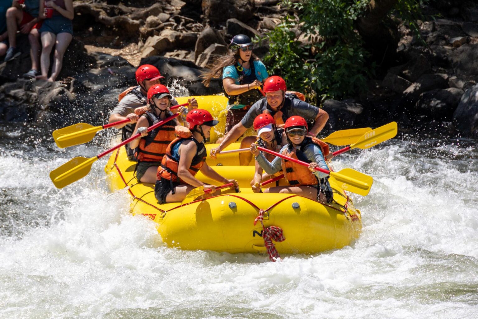 A yellow raft full of smiling people as they get ready to paddle through a rapid on the South Fork American River.