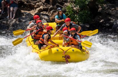 A yellow raft full of smiling people as they get ready to paddle through a rapid on the South Fork American River.