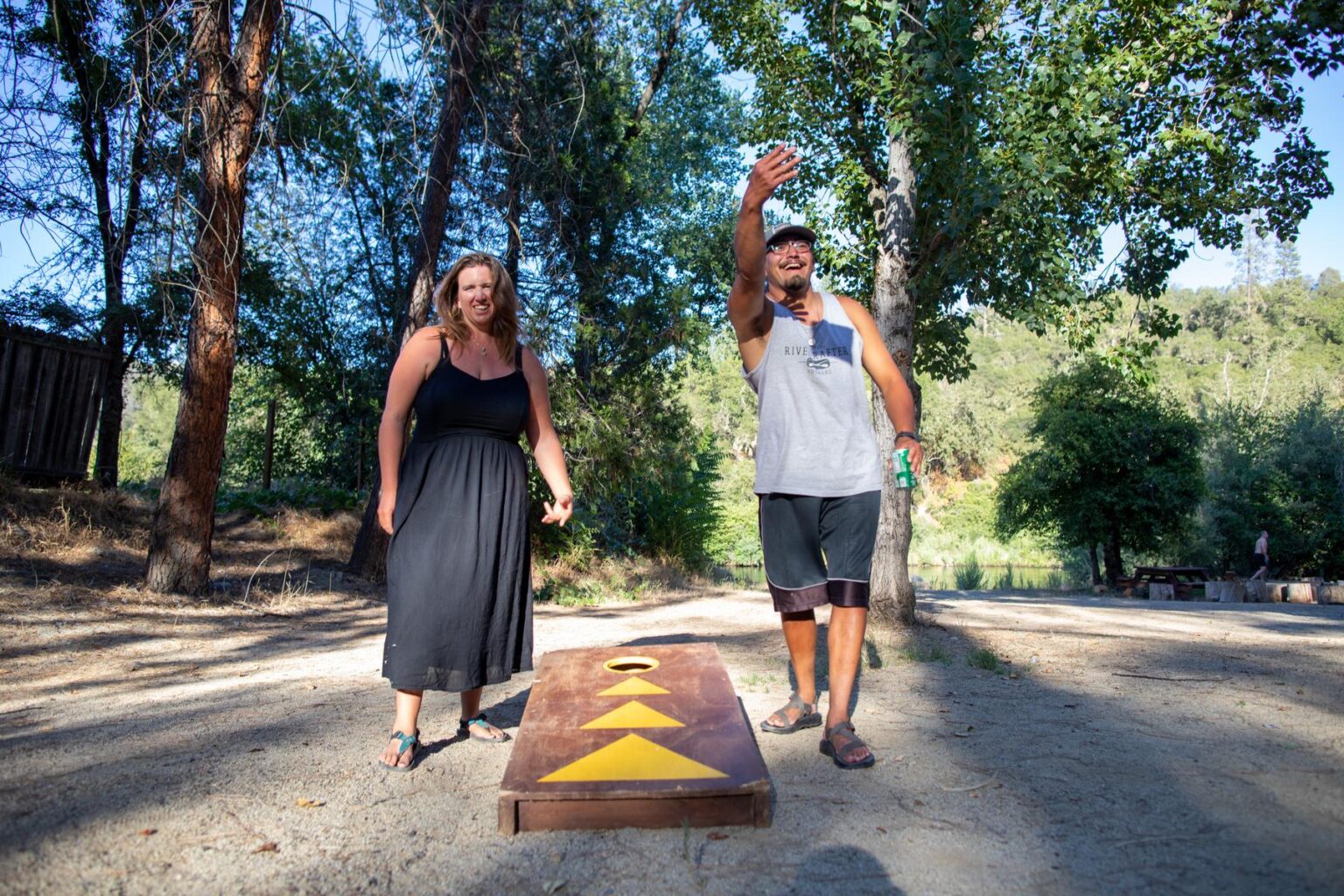 A couple plays cornhole amongst the trees at the OARS at EarthTrek campground.