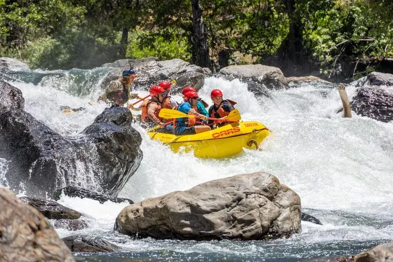A yellow raft maneuvers through a boulder-strewn channel with churning whitewater on California's Tuolumne River