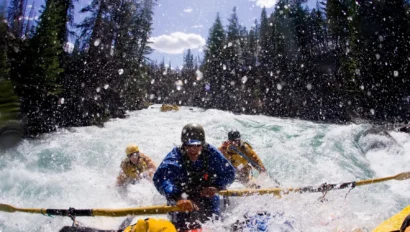 A person rows an oar raft while two passengers paddle agressively through a torrent of whitewater.