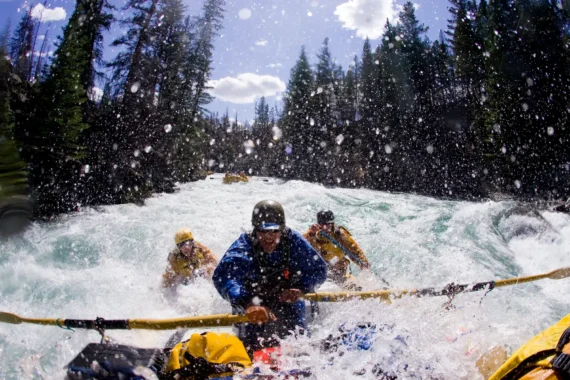 A person rows an oar raft while two passengers paddle agressively through a torrent of whitewater.