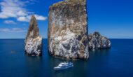 A luxury yacht in front of massive rocks coming out of the ocean in the Galapagos.