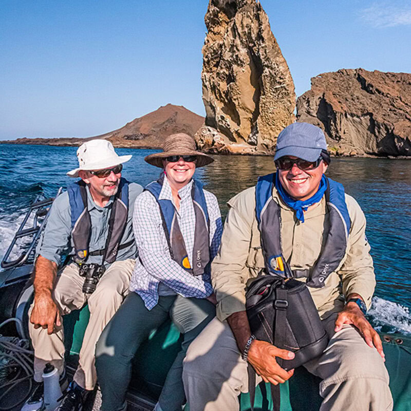 A guide and two guests aboard a pango speeding away from the rock spire at Bartolome Island Galapagos