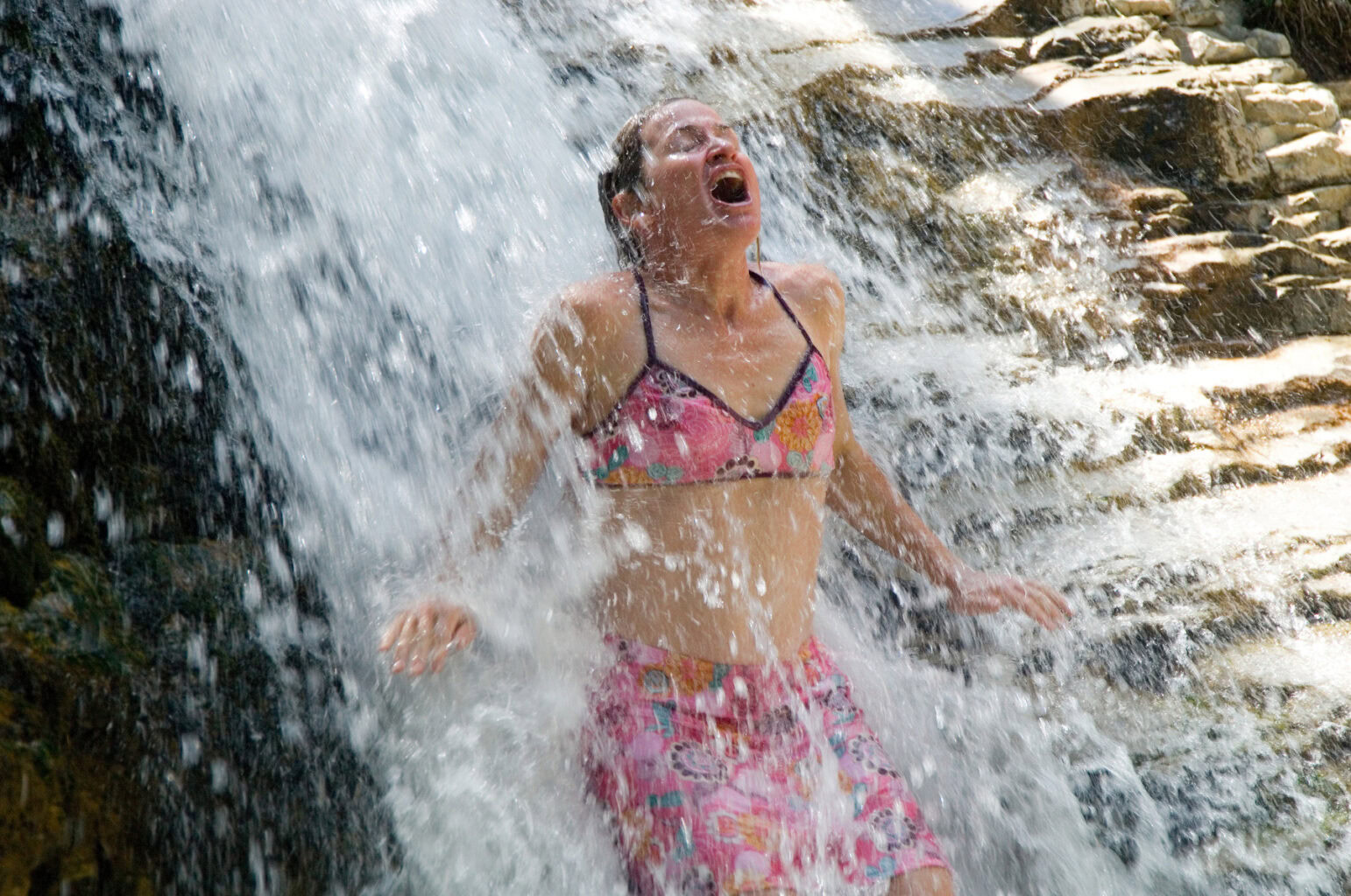 A woman stands under a waterfall
