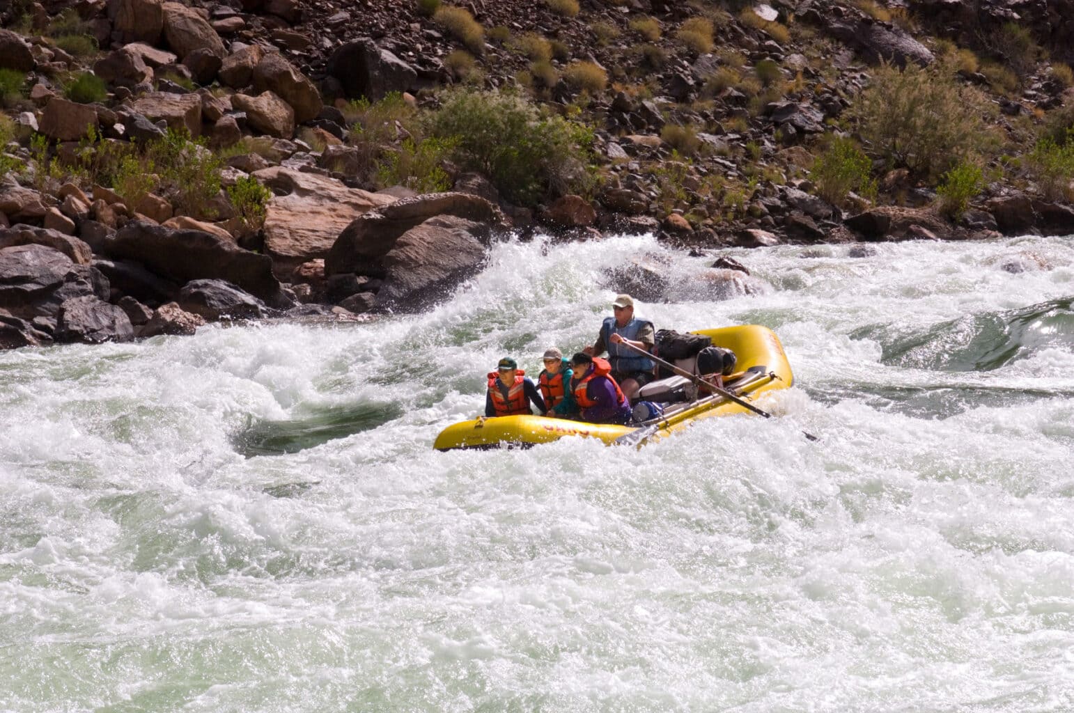 A river guide navigates three guests through the large waves of Hermit Rapid on the Colorado River in Grand Canyon.