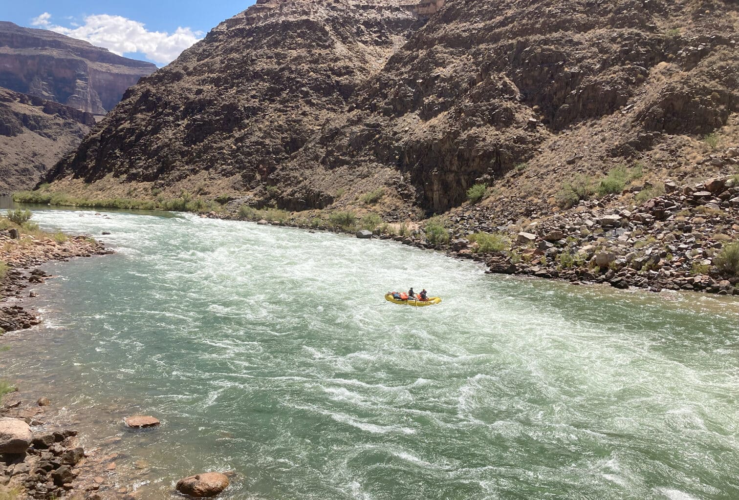A lone yellow raft with several people on board floats through Dubendorf Rapid in Grand Canyon. 
