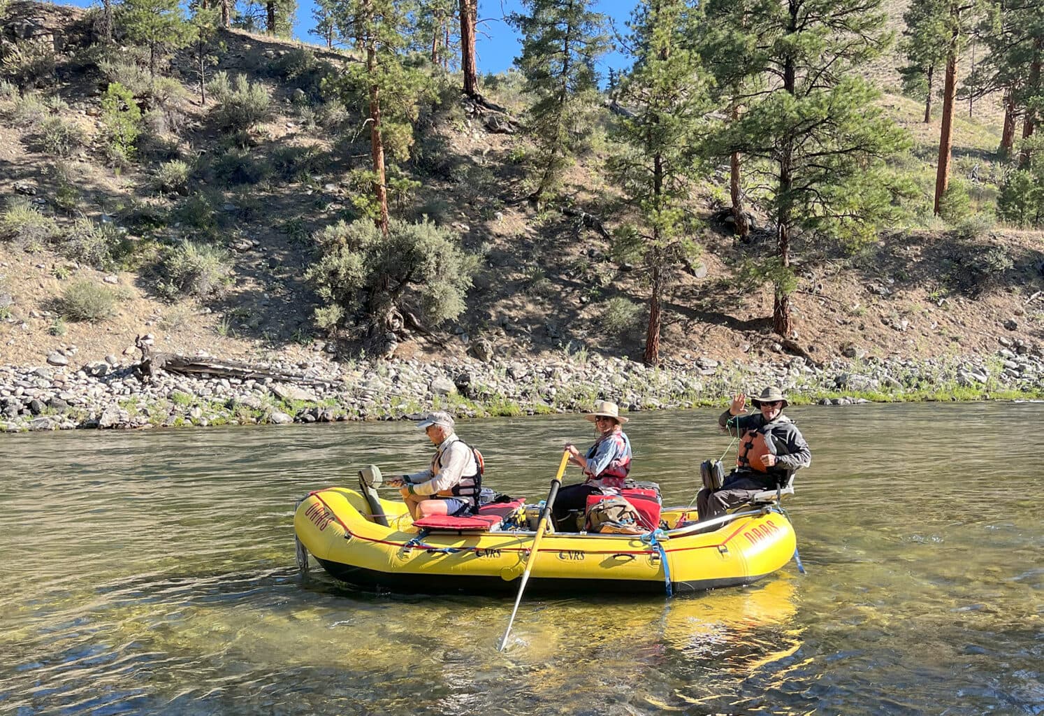 A raft guide floats downstream with two fishermen fishing from the front and back of the raft