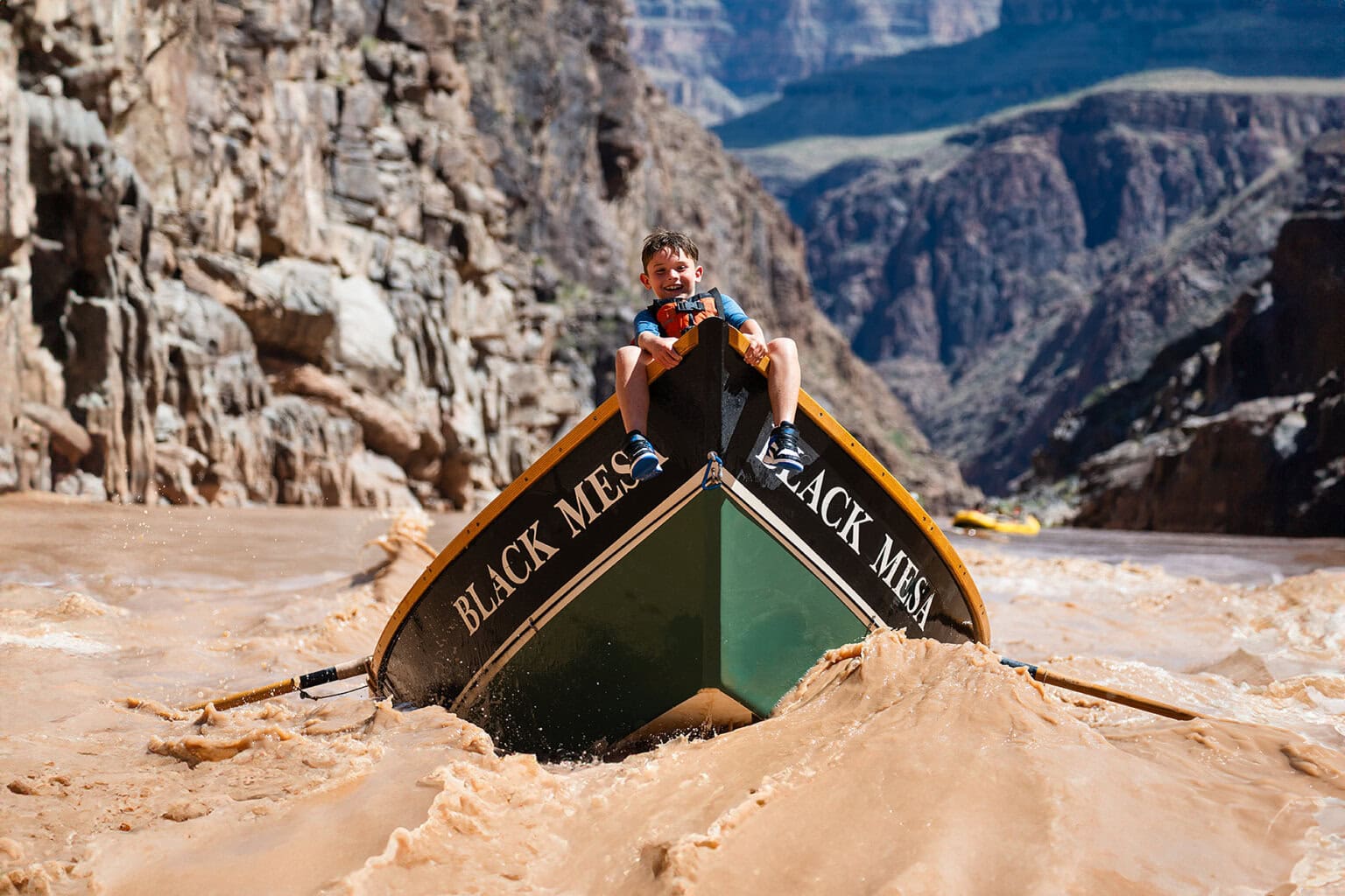 A young boy rides the bull of a dory through ripples on the Colorado River in Grand Canyon