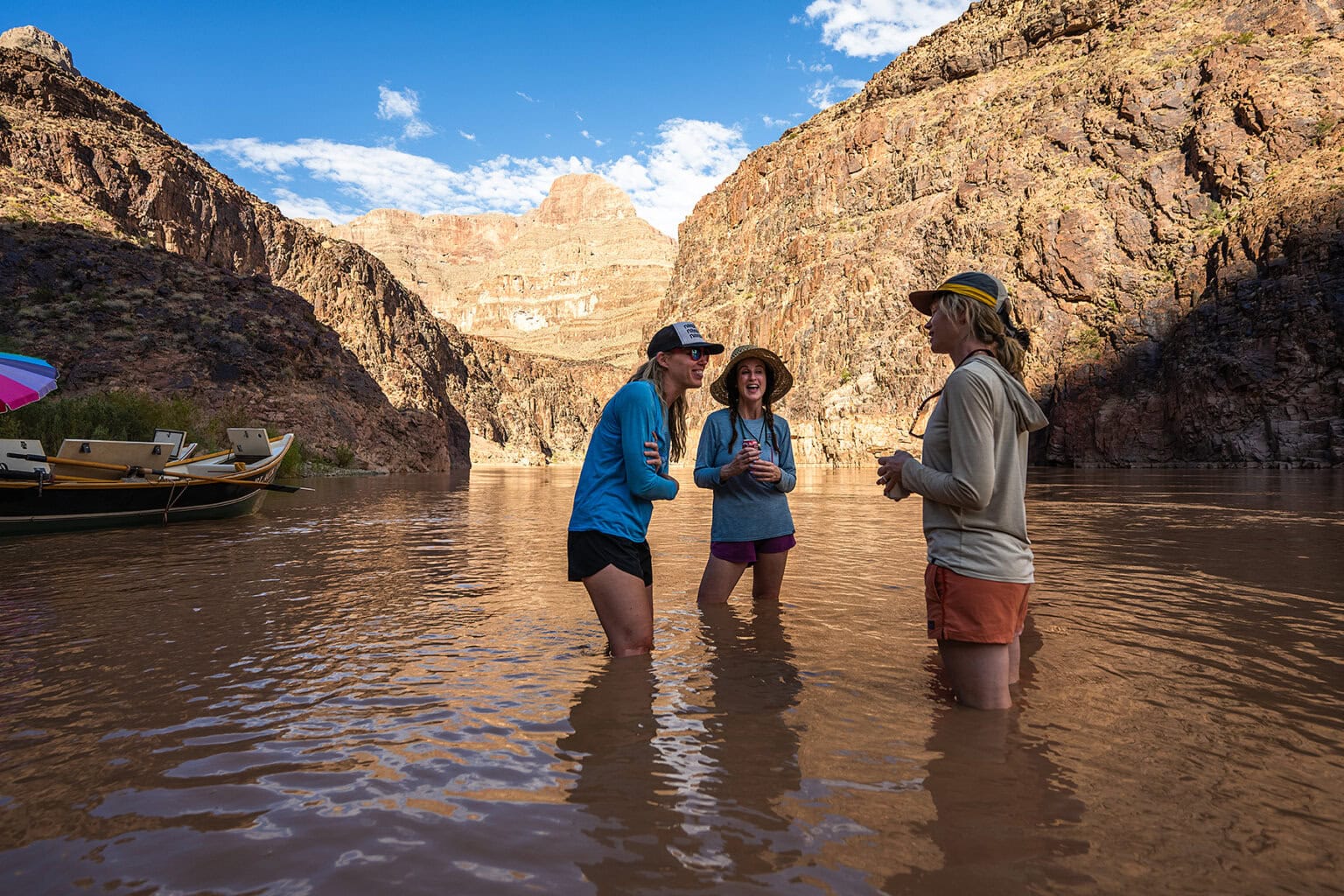 Three women stand in the Colorado River and laugh as they relax at camp in Grand Canyon