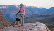 A mom and daughter hold on to each other as they look out over a vast canyon on the rim of Grand Canyon