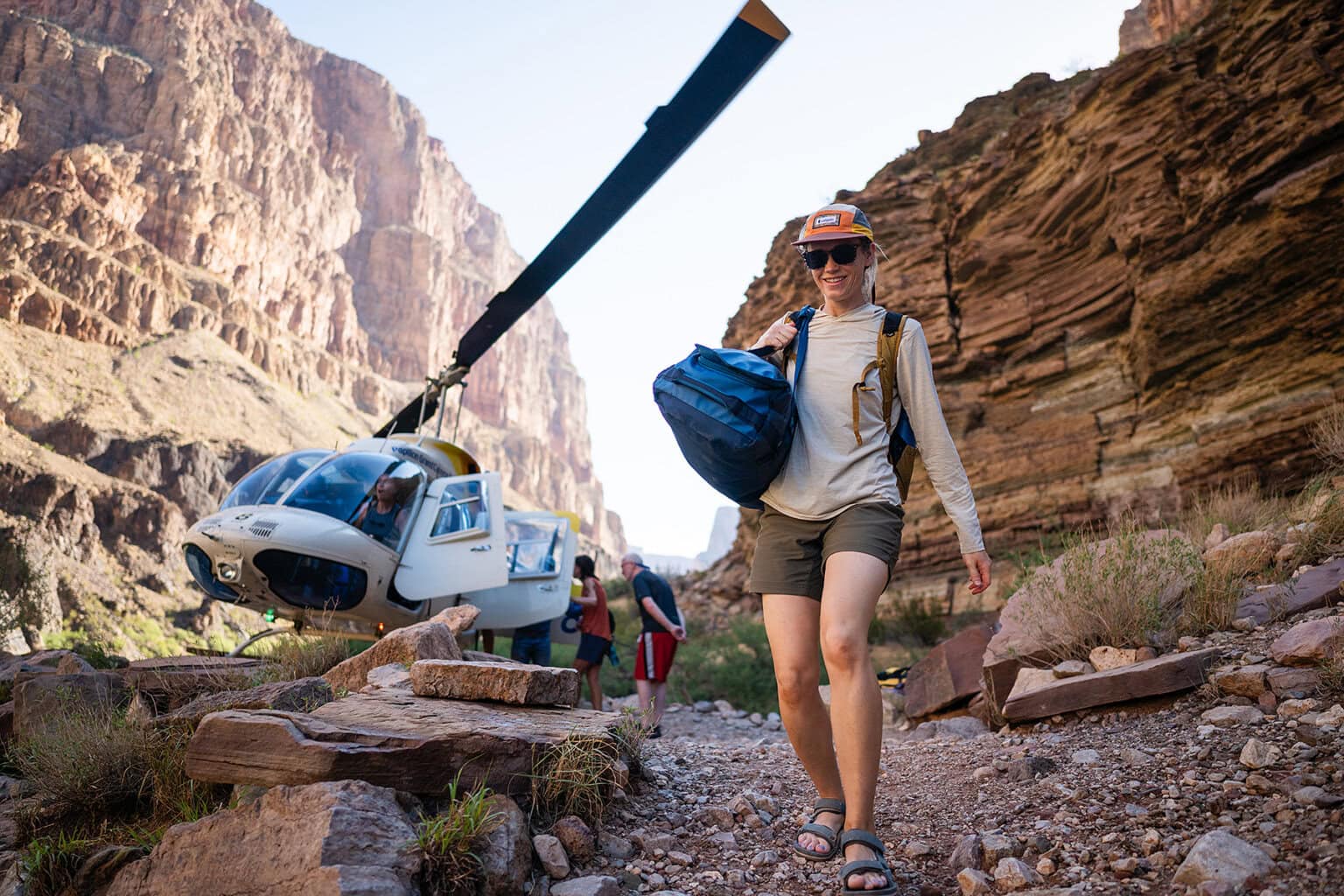 A woman carries her gear down a path after disembarking a helicopter at Whitmore Wash in Grand Canyon