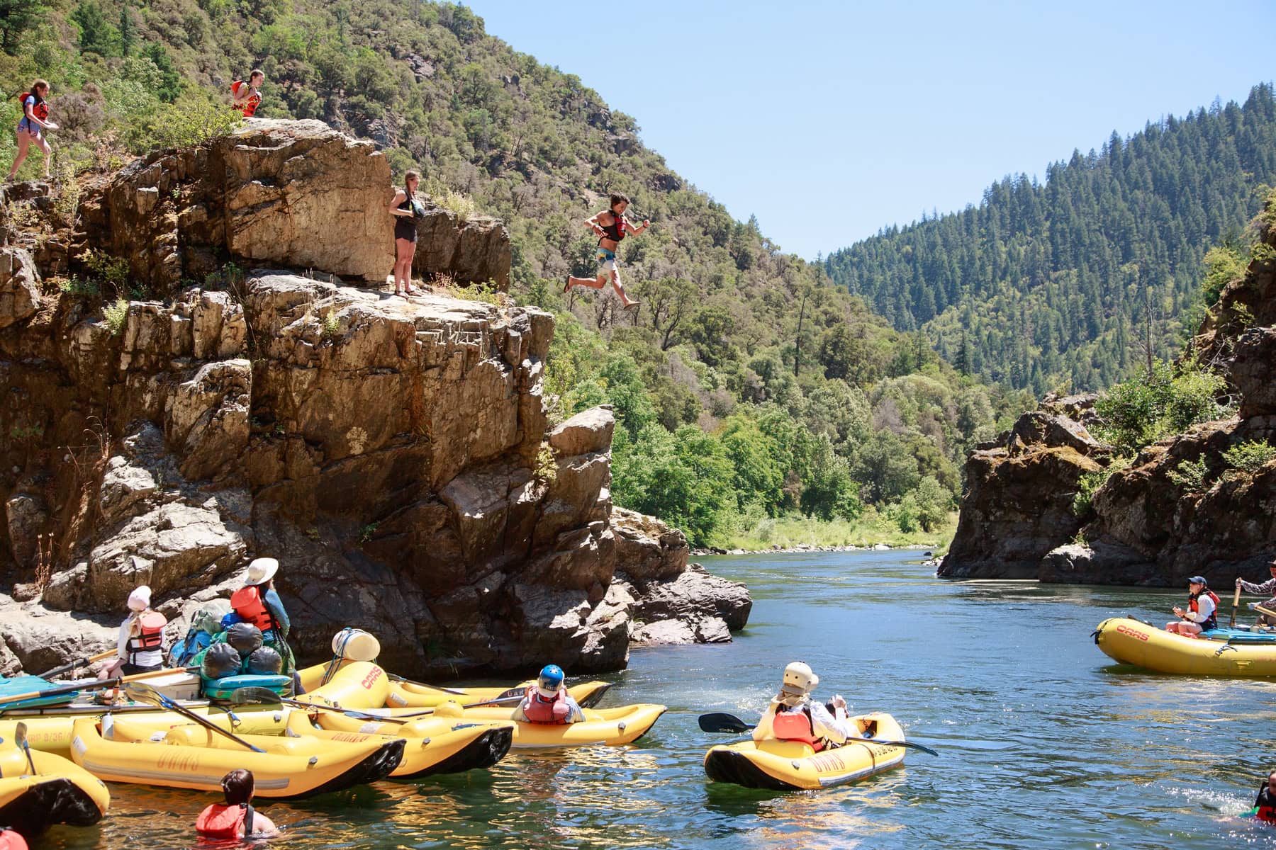 People in kayaks and rafts watch as other guests jump off a giant rock into the Rogue River in Oregon
