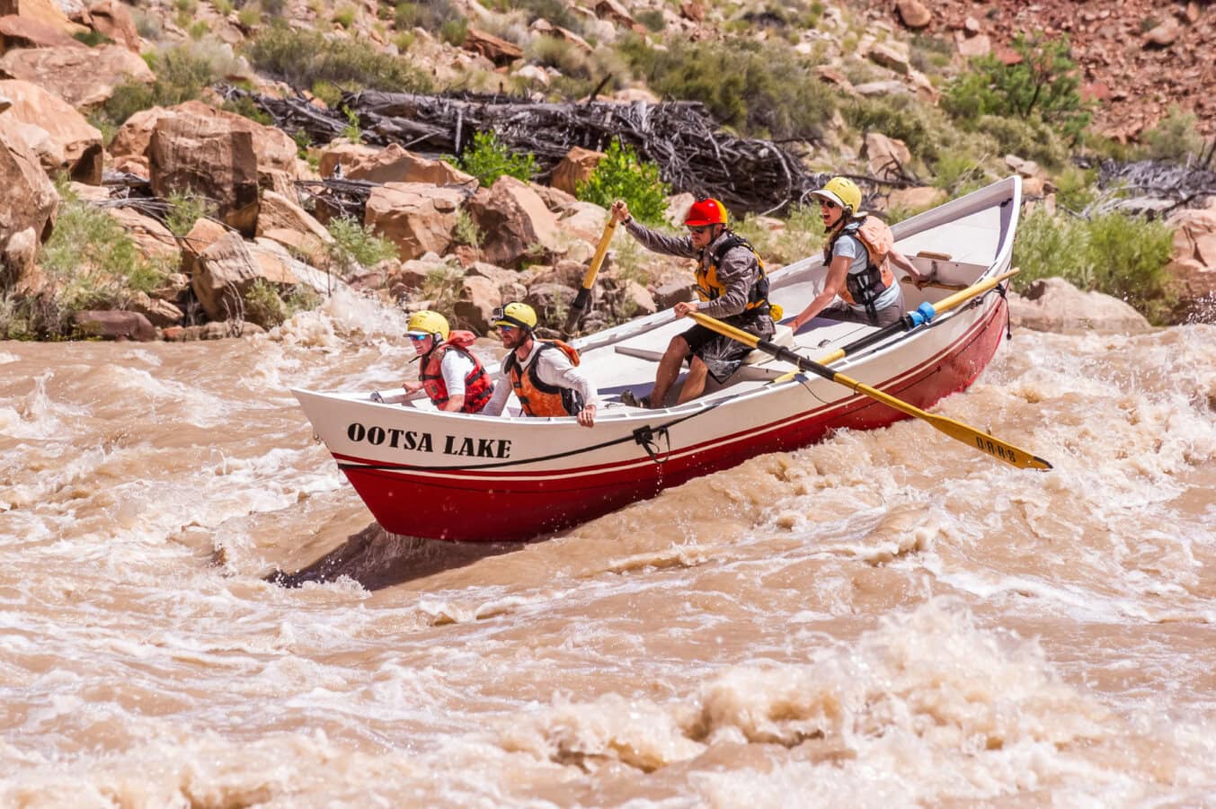 A guide rows three guests down the Colorado River through Cataract Canyon in a dory