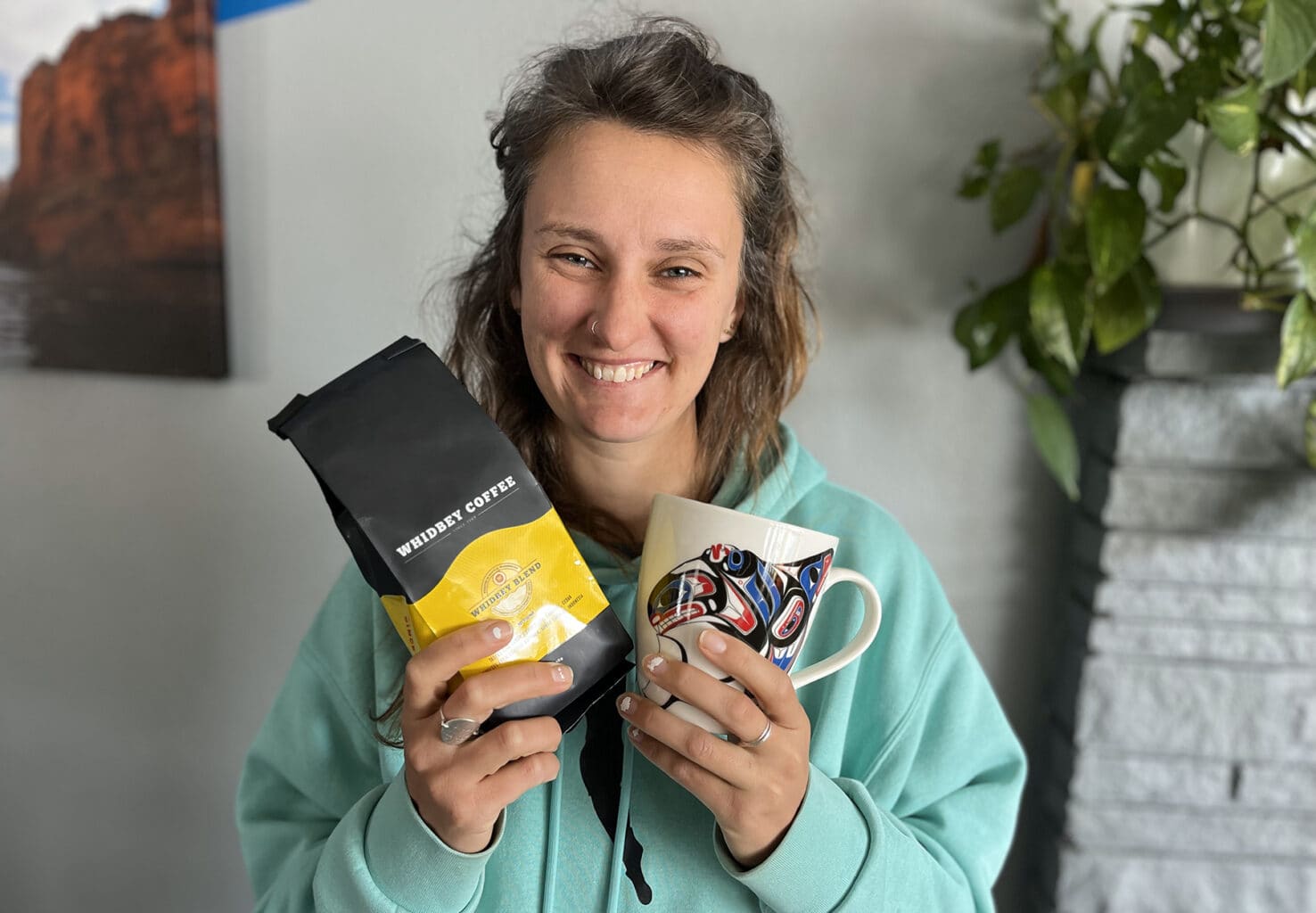 A woman holds a handmade mug and bag of coffee in her hands as she smiles for the camera