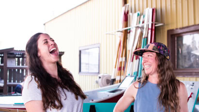Two women laughing in an airy boathouse setting