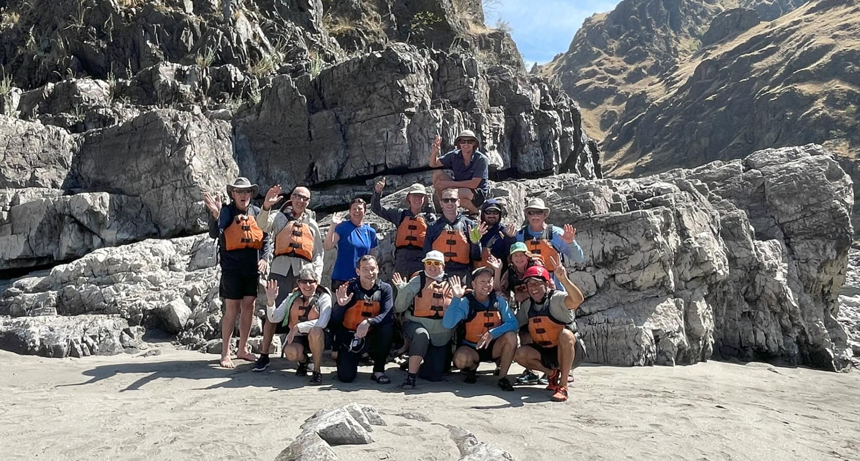 A group of people posing together outdoors in front of a rocky cliff under a clear blue sky.