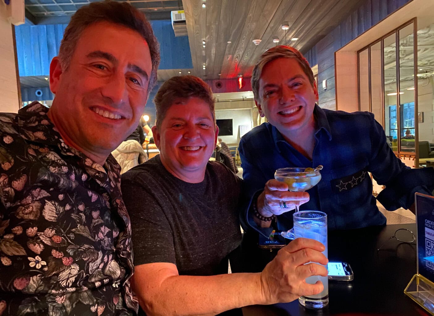 Three friends smile and enjoy drinks together at a warmly lit indoor setting