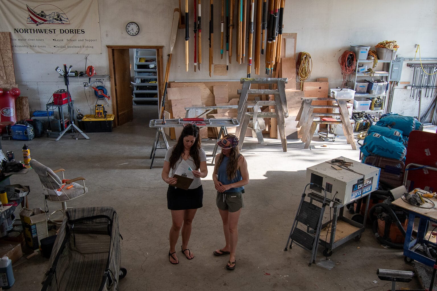 Two women review paperwork together in a warehouse setting at OARS Dories Idaho