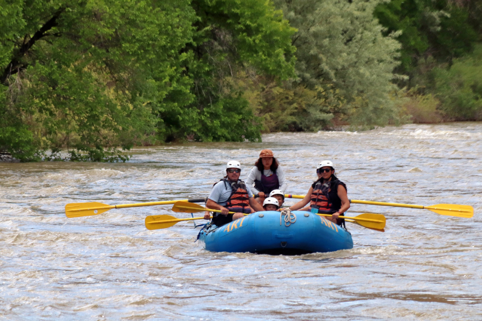 A river guide navigates a blue raft with a family of rafters down Cottonwood Canyon, one of Colorado's best rafting day trips