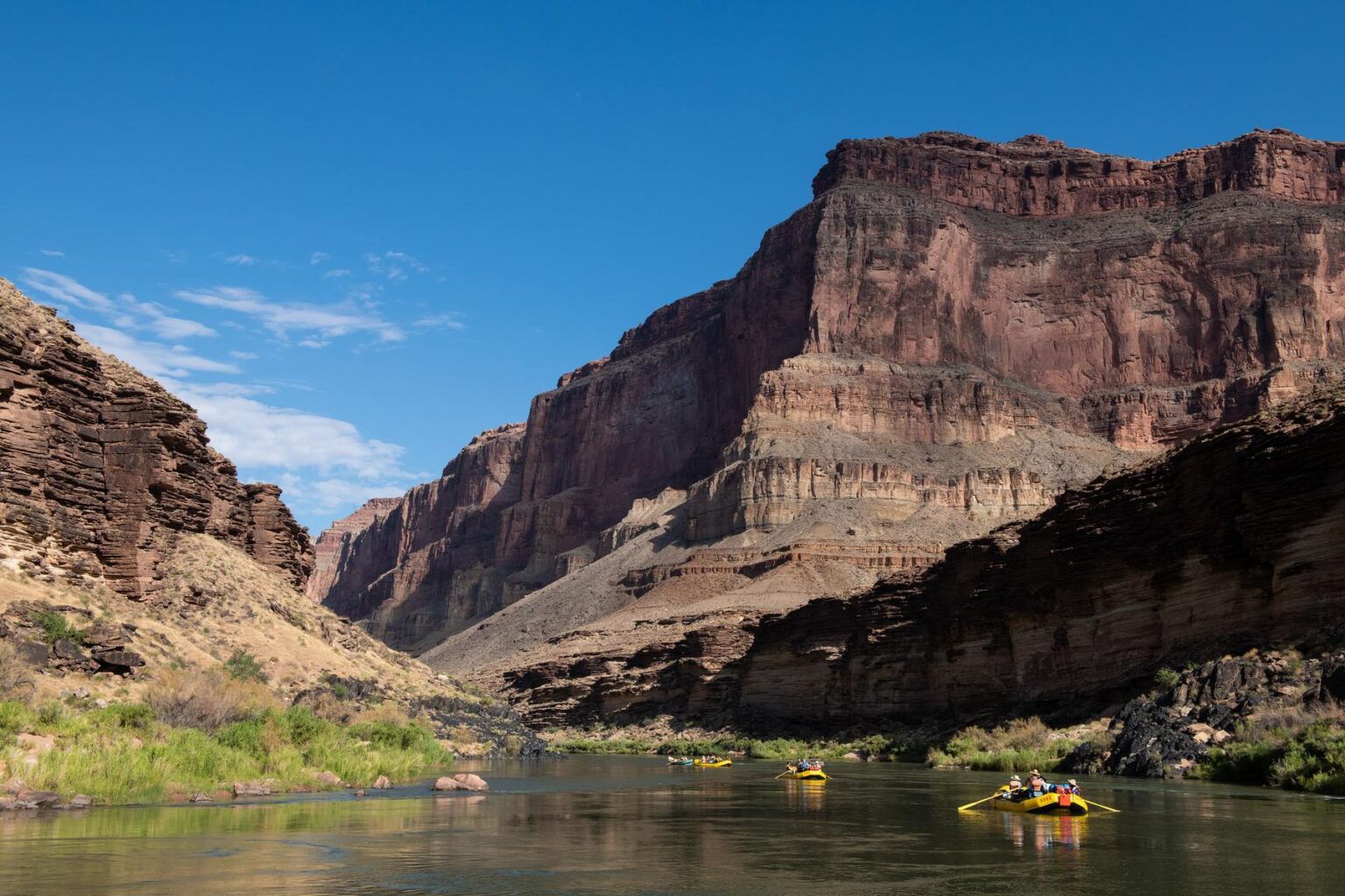 Three yellow rafts flow on a green-blue stretch of the Colorado River in Grand Canyon 