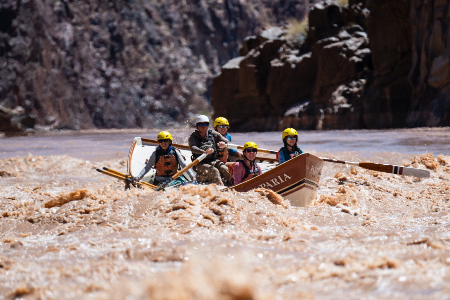 A dory guide navigates whitewater on a silty brown stretch of the Colorado River.