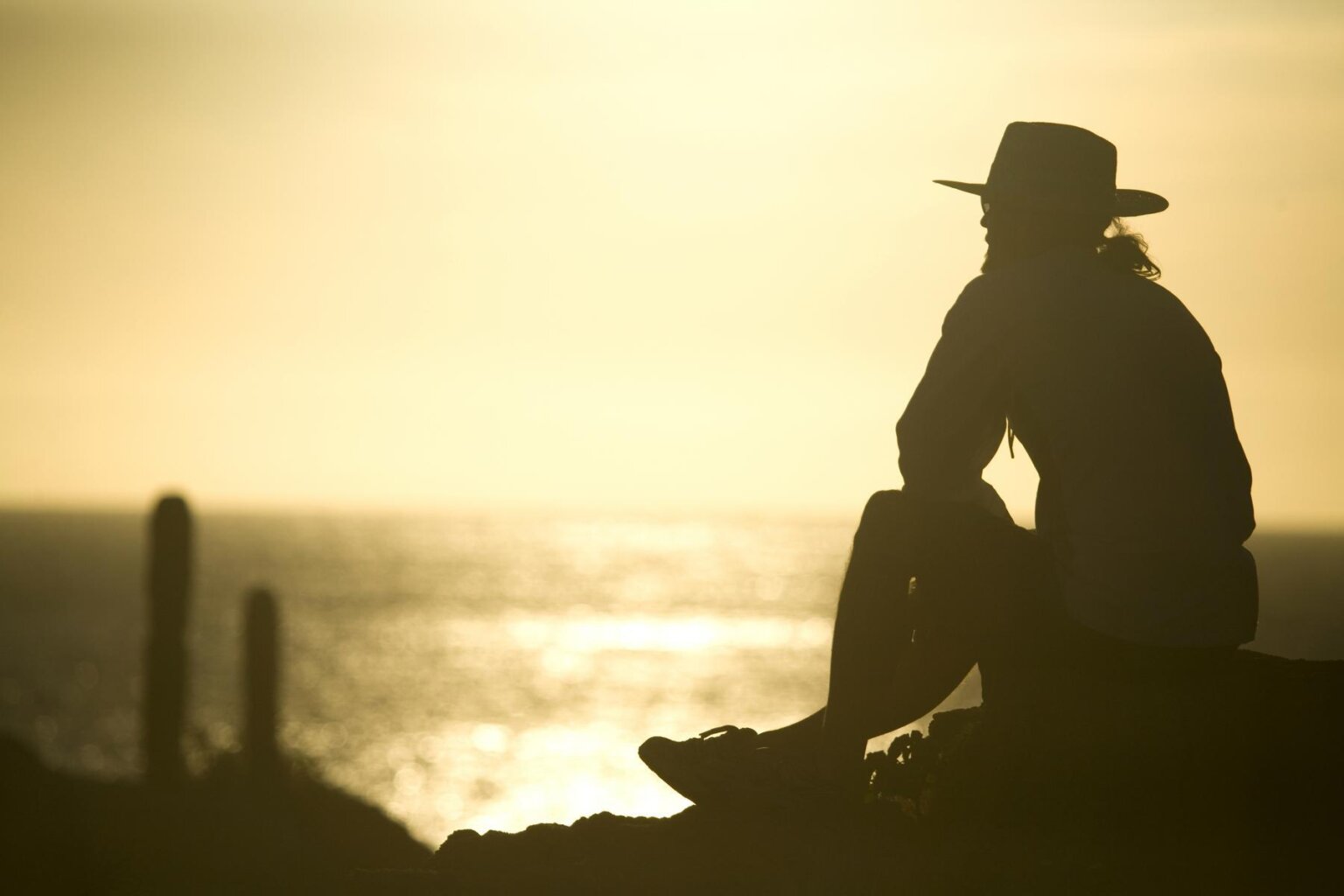 A man with a hat sits on a ledge near the coast in Baja.