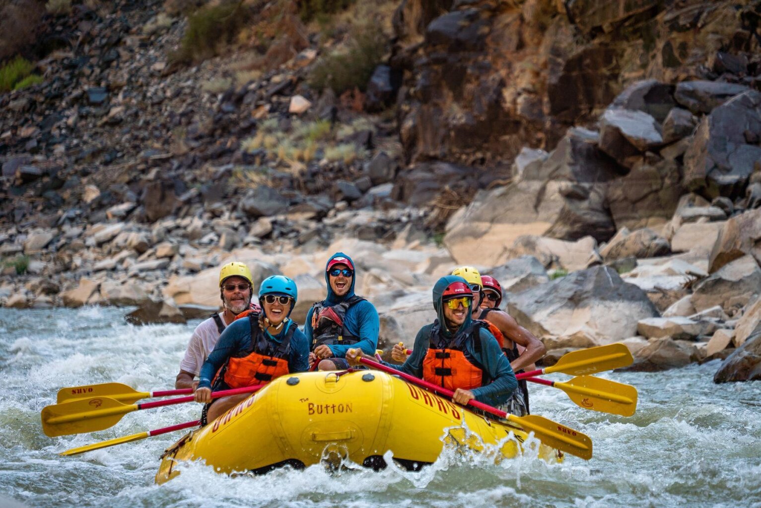 A group of adults smile for the camera while paddling down the Colorado River in Westwater Canyon