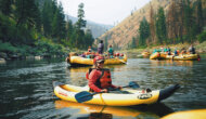 A woman wearing a PFD and helmet sits in an inflatable kayak amongst a group of yellow rafts on the Main Salmon River