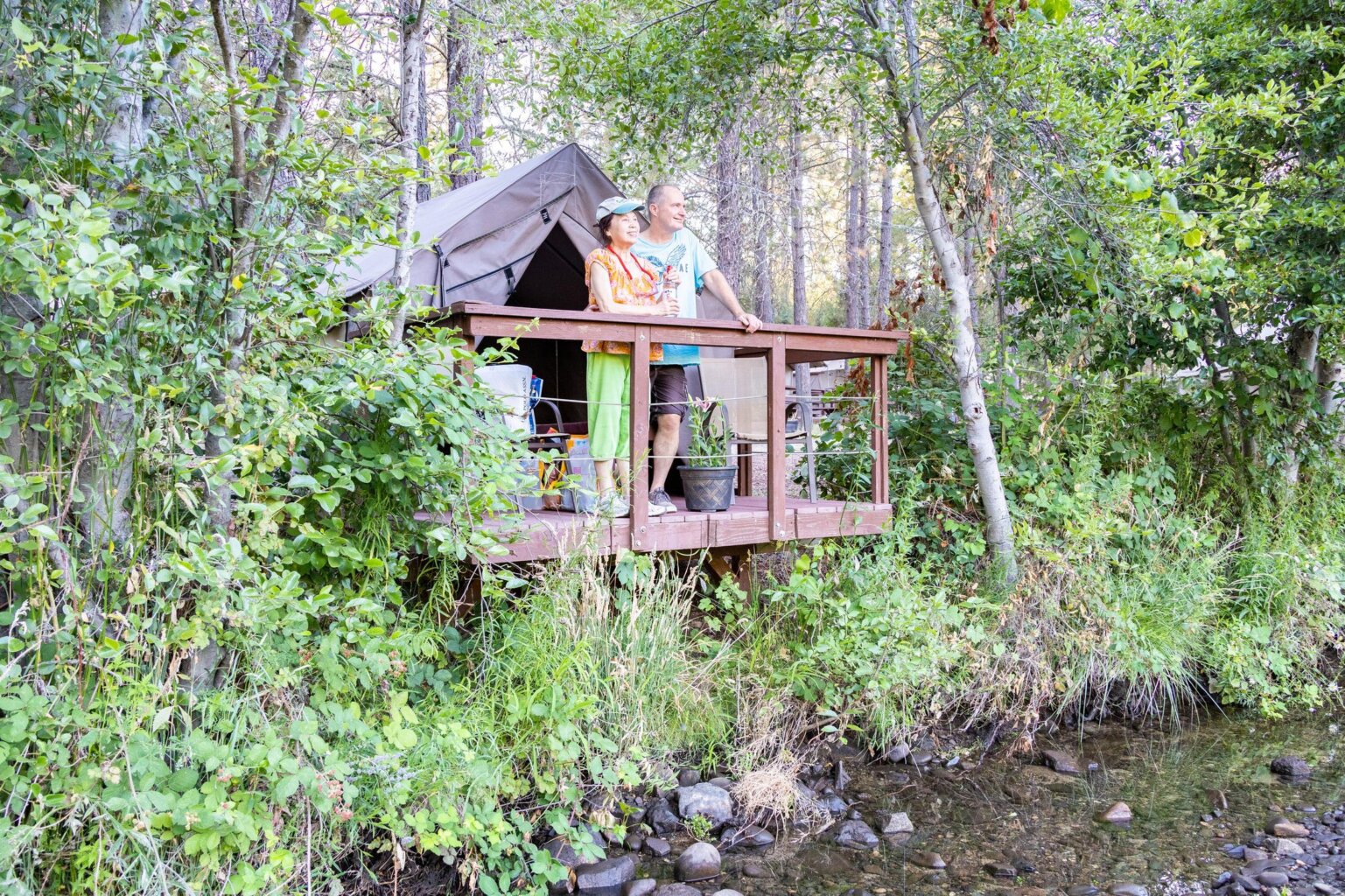 Two people stand on the deck of their canvas tent cabin and look out at the American River which runs right by the cabin.