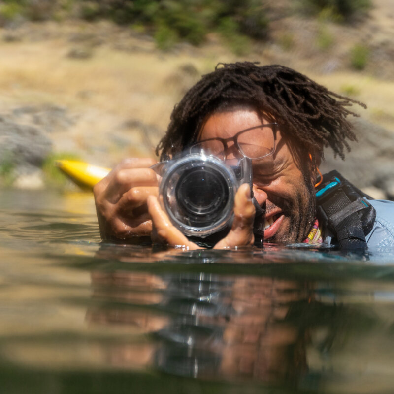 A person submerged in a river shooting photos with a waterproof camera